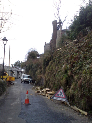 Cones and a road works sign set out on a lane while the bank above is cut back