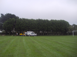 A tree line cleared beside a playing field, with the work vehicle parked up